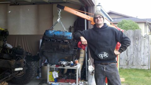 1978 Ford Bronco - A person stands next to an engine that is suspended by an engine hoist, likely during a motor rebuild.