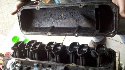 1978 Ford Bronco - A person holds a greasy valve cover over an engine block, revealing the valve train.