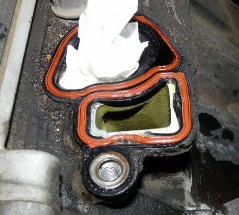 1999 Ford Crown Victoria - Close-up of an engine intake manifold gasket, showing the orange seal and an opening stuffed with a paper towel.