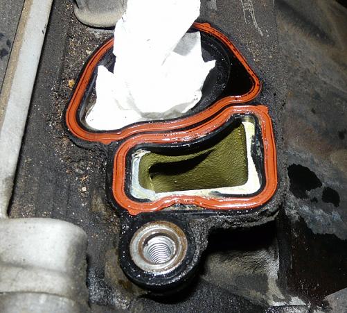 Engine intake manifold gasket with orange seal, paper towel stuffed inside opening