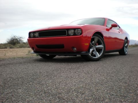 2010 Dodge Challenger - A red Dodge Challenger is parked on a gravel road with a dry, desert-like landscape in the background.