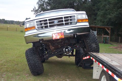 1995 Ford Bronco - Head-on view of a heavily lifted white-over-green Ford Bronco with its solid front axle articulated, showing coil springs, long shocks, a c…