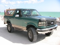 1986 Ford Bronco - This Ford Bronco is parked on a sandy area with the ocean in the background.
