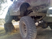 1986 Ford Bronco - The rear wheel of a heavily soiled 1980s Ford Bronco is lifted onto a rock.