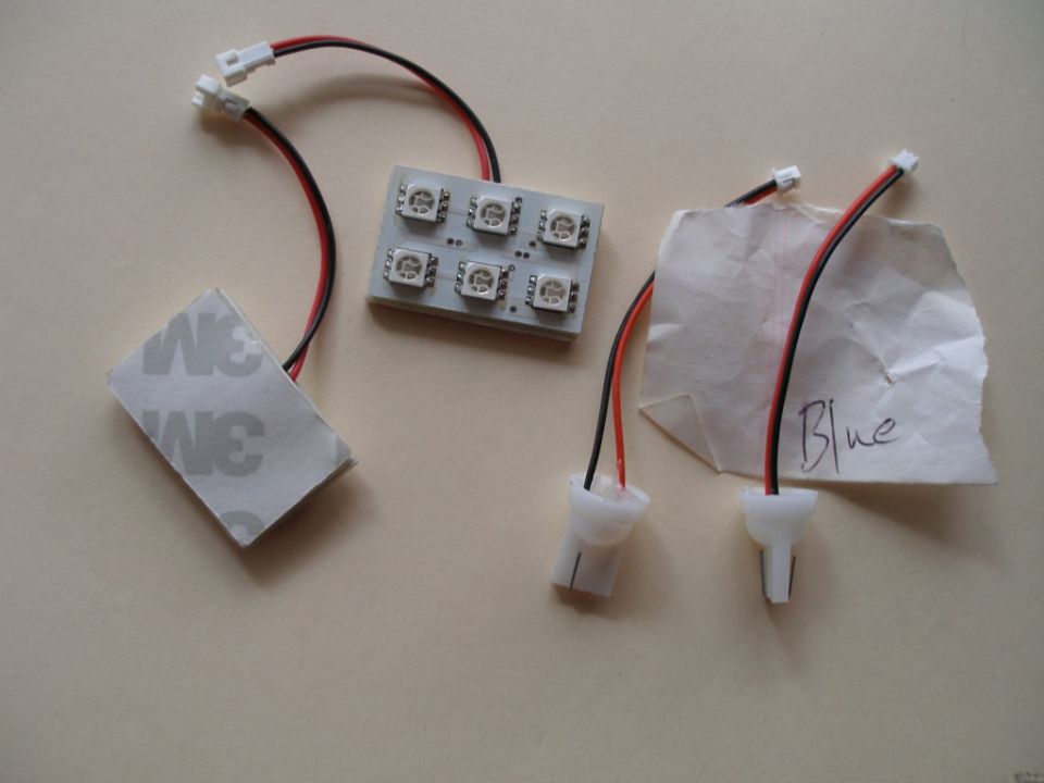 LED strip with six LEDs, red and black wires, and 3M adhesive backing. A piece of paper with 'Blue' written on it is nearby