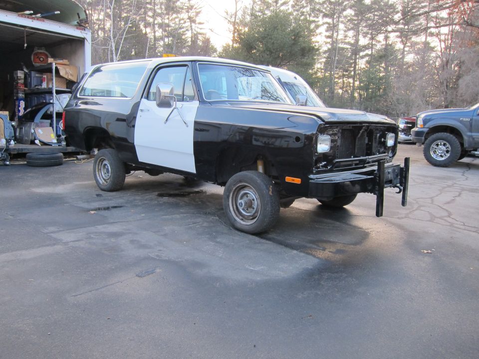 Black and white SUV with missing grille, parked outside a garage