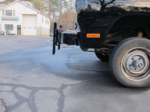 1987 Dodge 1500 - A close-up view of the rear bumper and wheel of a black pickup truck parked outside a salvage yard.