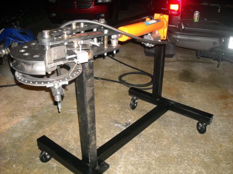 1979 Ford F-150 - A heavy-duty tube bender with an orange hydraulic cylinder is set up on a wheeled stand, with vehicles visible in the background.