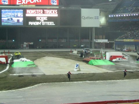 1986 Ford Bronco - Monster trucks are performing in an indoor arena with a large crowd watching.