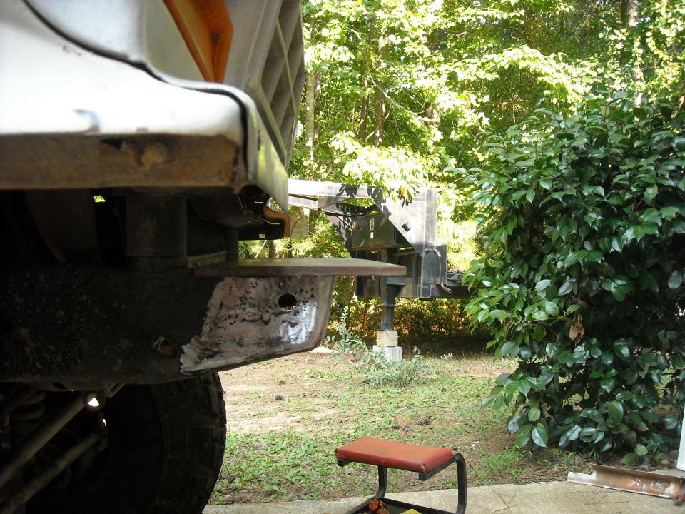 Close-up of a truck's front bumper area, showing metalwork and repair. A red stool is nearby