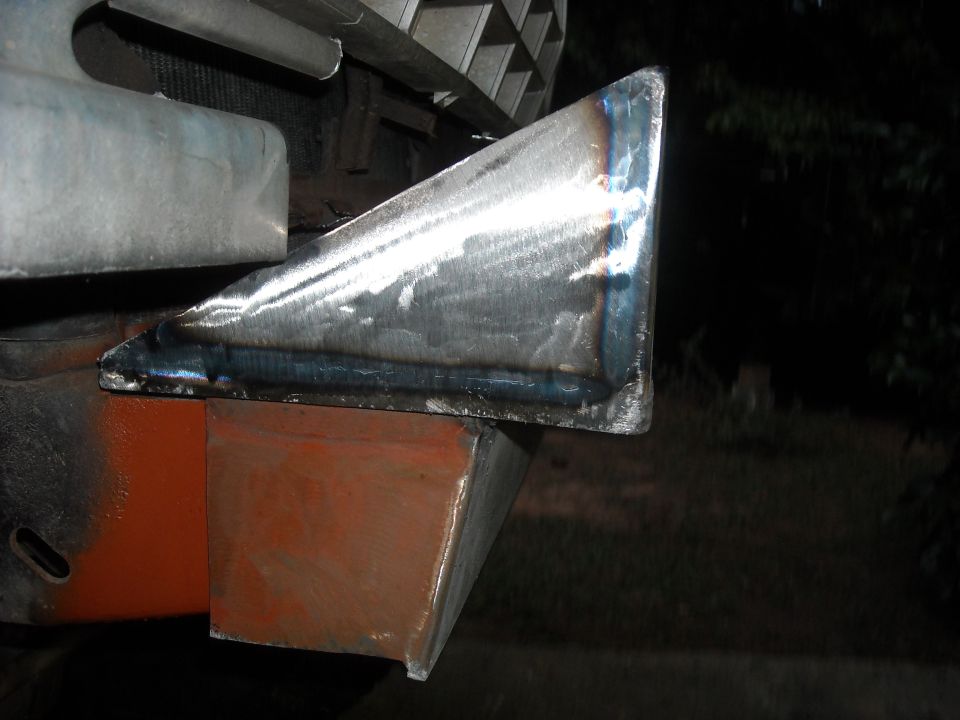 Close-up of a welded metal triangular piece attached to an orange-painted metal block, part of a vehicle bumper