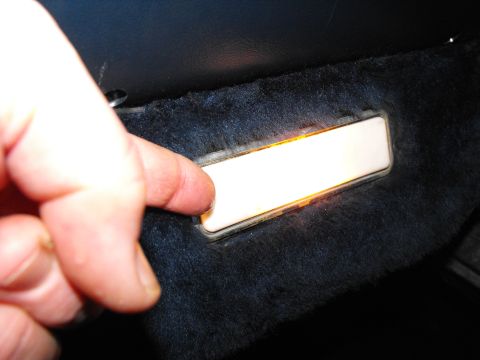 1986 Ford Bronco - A finger activates a lit interior door light, set within a dark, carpeted panel.