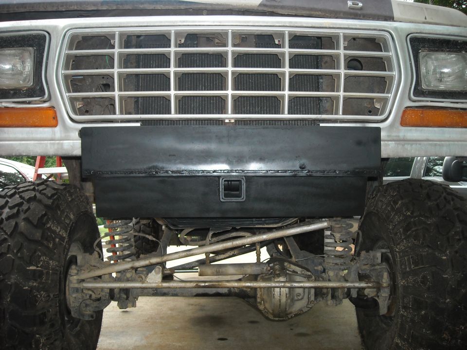 1979 Ford F-150 front grille and bumper with a black toolbox mounted on it. Large off-road tires are visible