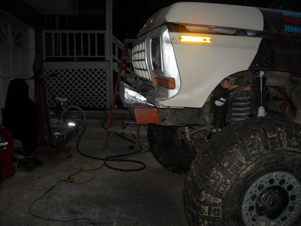White lifted Ford F-150 front corner in garage at night, bumper off, big muddy tires