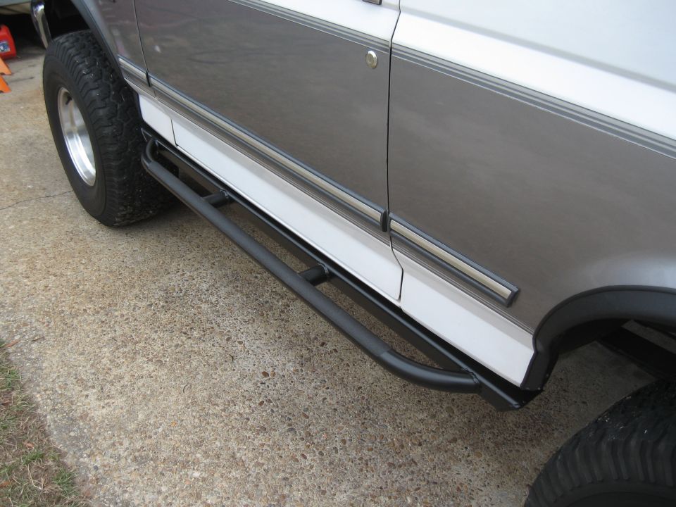 Side view of a gray and white truck with black tubular running boards and off-road tires