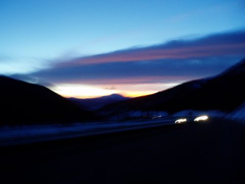 2009 Kenworth T800 - Headlights blur on a highway as the sun sets, painting the sky with vibrant colors.