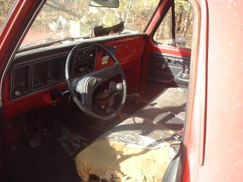 1993 Ford Bronco - The interior of a red truck cab, a worn plaid seat and a dashboard with a radio and steering wheel.