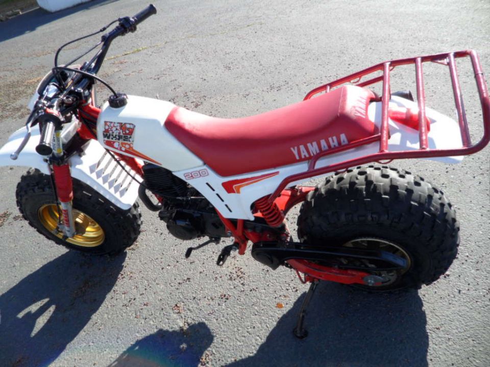 White and red Yamaha 200 three-wheeler with gold rims and a rear cargo rack, viewed from the front-right