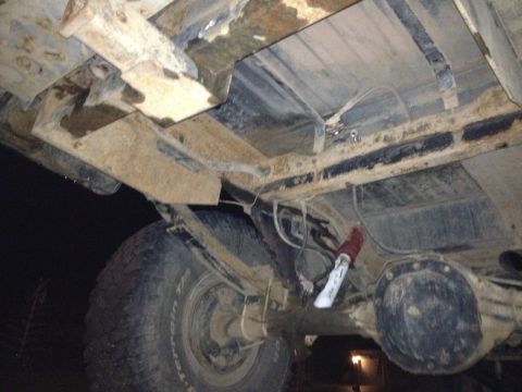 1995 Ford Bronco - The underside of a vehicle shows its rear axle, suspension, and fuel lines, covered in dirt and grime.