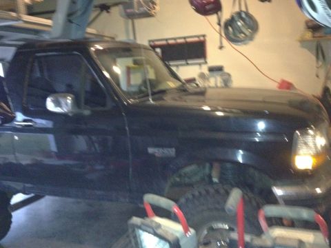1995 Ford Bronco - A dark SUV, possibly a Ford Bronco, is parked indoors with its front quarter visible.