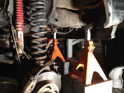 1995 Ford Bronco - Vehicle's undercarriage is supported by jack stands, revealing suspension and brake parts.