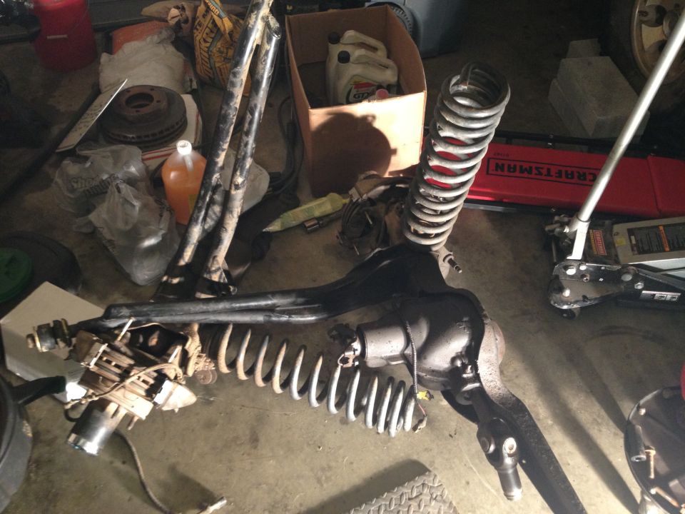 Removed front axle with coil springs and radius arms on garage floor