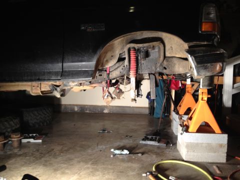 1995 Ford Bronco - The rear suspension of a Ford Bronco is being worked on while the vehicle is supported by jack stands in a garage.
