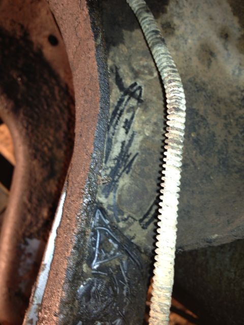 1995 Ford Bronco - Close-up of a rusty metal component with markings and a ribbed hose, likely part of a vehicle's undercarriage.