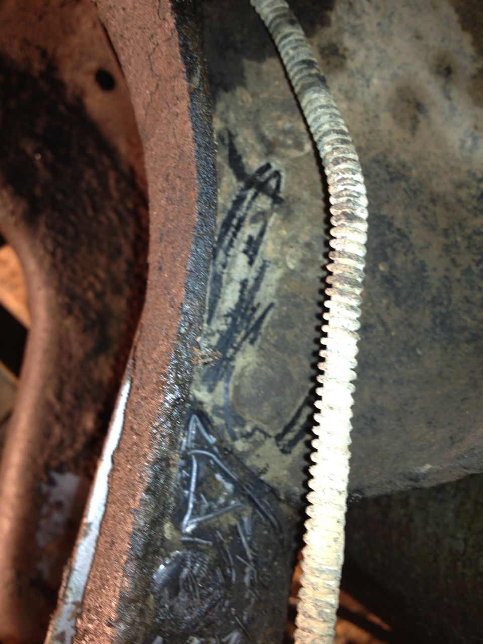 Close-up of a rusty metal part with black markings and a ribbed hose attached