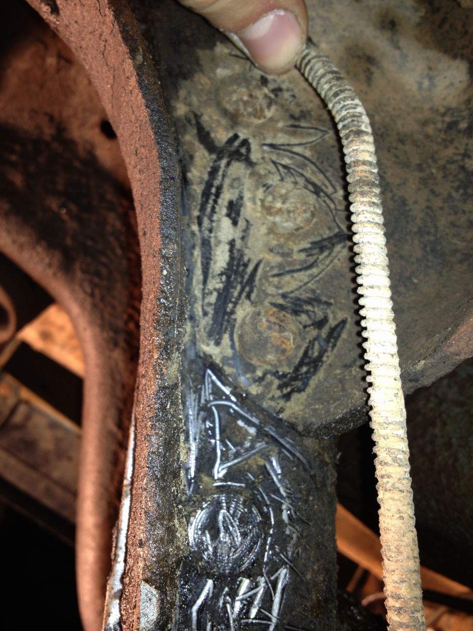 Close-up of rusty metal undercarriage part with white markings and a ribbed cable
