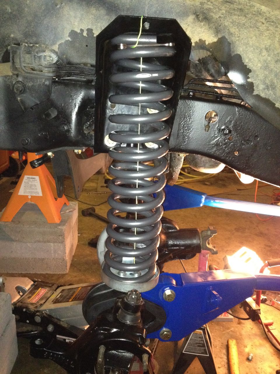 Front suspension coil spring assembly with black painted frame and blue suspension components. Jack stands support the vehicle