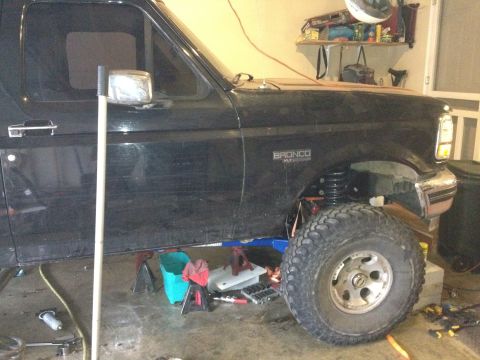 1995 Ford Bronco - A black Ford Bronco is shown from the side with its front tire and suspension visible. The vehicle appears to be undergoing maintenance or…