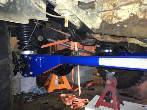 1995 Ford Bronco - The vehicle's undercarriage is supported by jack stands, revealing modified suspension parts and the frame.