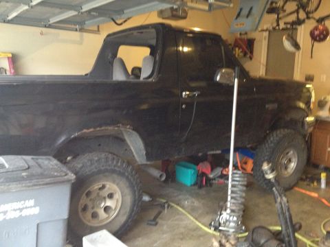 1995 Ford Bronco - A black Ford Bronco is undergoing maintenance in a garage, with tools and parts scattered around.