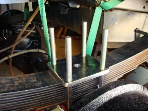 1995 Ford Bronco - Close-up view of a U-bolt plate being installed on a vehicle's rear axle leaf spring.