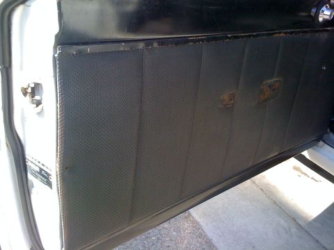 1964 Ford Ranchero - Interior door panel with perforated vinyl and two faded emblems. A "Ford" label is visible on the door jamb.