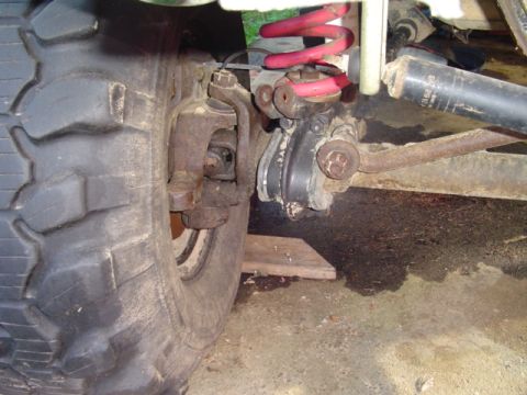 1993 Ford Bronco - Close-up of the front suspension and axle on a 1993 Ford Bronco, showing a red coil spring, a black shock absorber, a steering knuckle/ball…