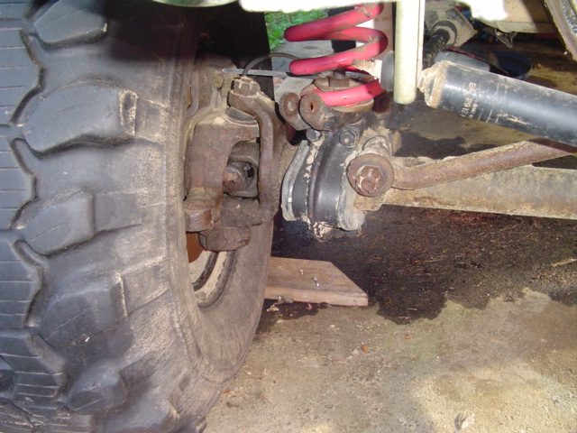 Front axle, red coil spring, shock, and knuckle under a lifted Ford Bronco
