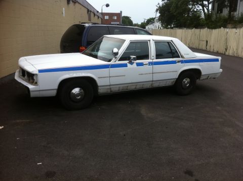 1991 Ford LTD Crown Victoria - This Ford Crown Victoria appears to be a former police or taxi vehicle, evident by its distinctive blue stripe.