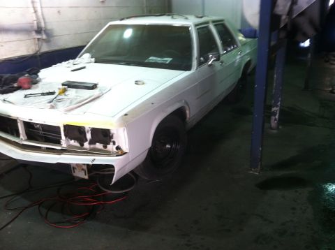 1991 Ford LTD Crown Victoria - A white 1991 Ford Crown Victoria LTD is parked in a garage, with its front end disassembled for repairs.