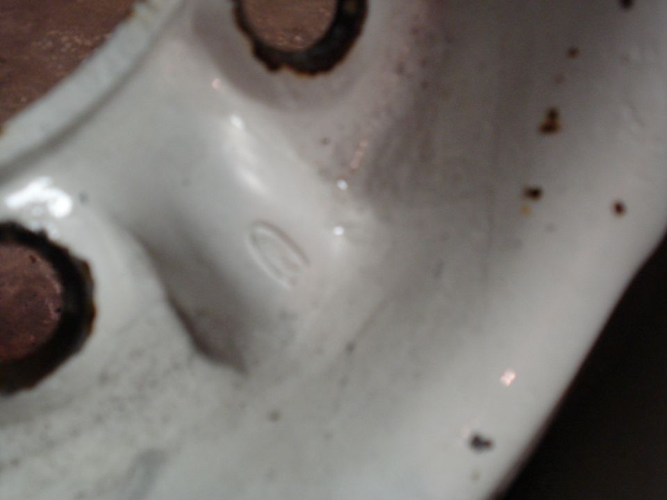 Close-up of a white painted metal part showing two bolt holes and a faint oval-shaped marking
