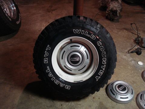 1967 Ford F-250 - A tire with 'Wild Country Radial RVT' text is shown with a Ford hubcap. Other hubcaps are nearby.