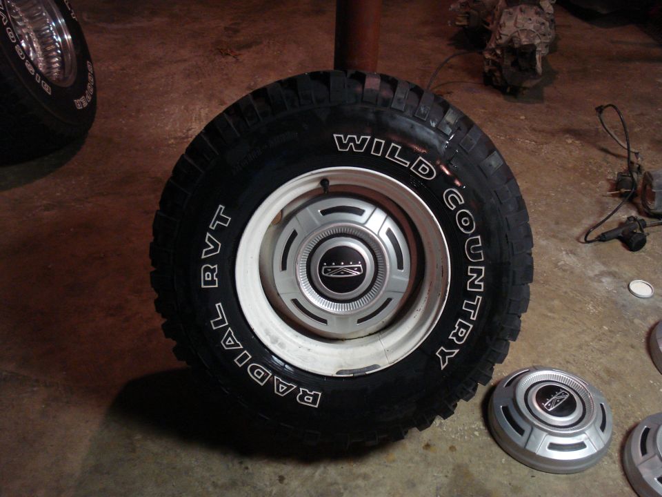 Close-up of a Wild Country radial tire on a white rim with a Ford hubcap. Another hubcap is on the floor