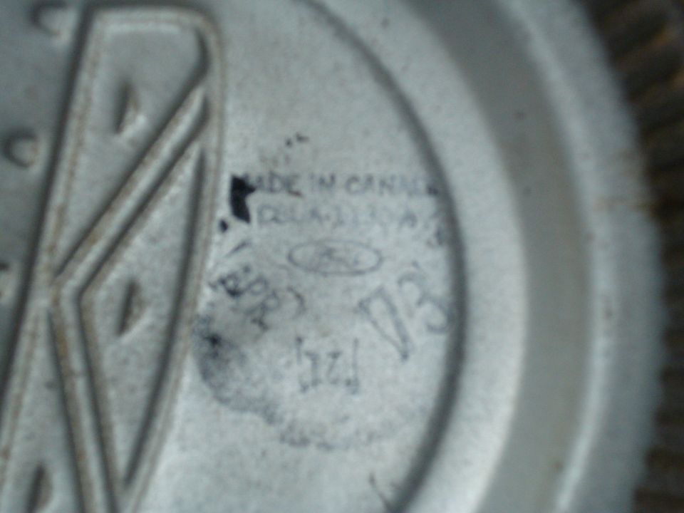 Close-up of a Ford emblem with 'MADE IN CANADA' and part numbers visible