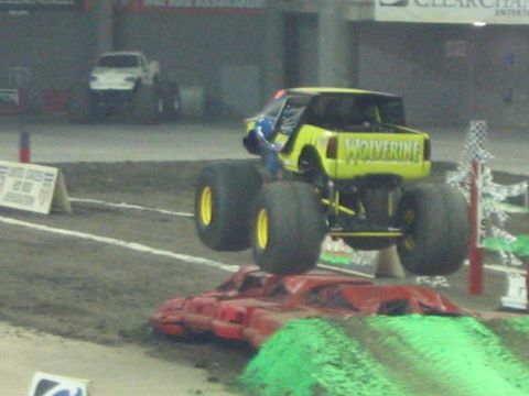 1986 Ford Bronco - A monster truck named Wolverine soars through the air during an event, with another vehicle visible in the distance.
