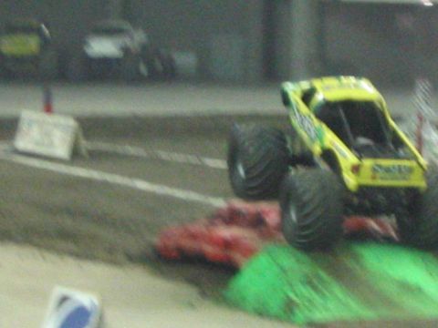 1986 Ford Bronco - A yellow monster truck with large tires is captured mid-air during a competition.