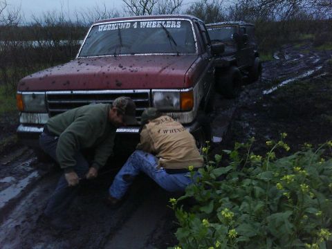1989 Ford Bronco - Two men attempt to winch a maroon 1989 Ford Bronco out of deep mud, with another vehicle visible behind.