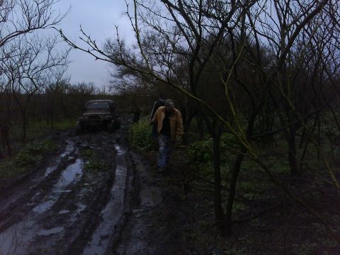 1989 Ford Bronco - An off-road vehicle is stuck in deep mud on a trail surrounded by trees.
