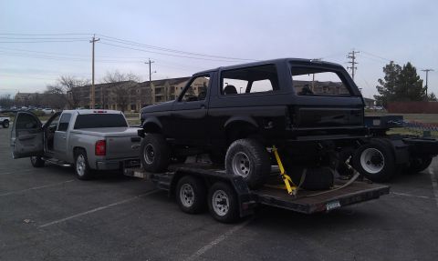 1995 Ford Bronco - A black Ford Bronco is loaded onto a trailer, being towed by a silver pickup truck.