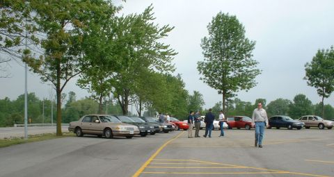 2000 Ford Crown Victoria - Cars parked in a lot with people milling around on a cloudy day.
